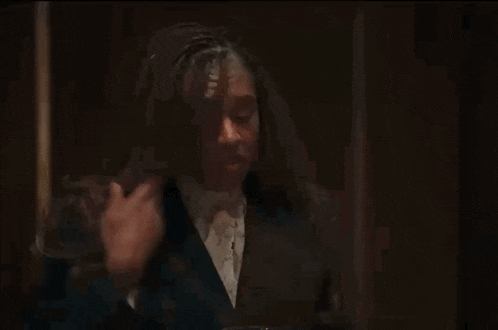 a woman in a suit is standing in a dark room and holding her hair .