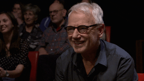 a man sitting in a theater laughing with the words ok tot hier behind him