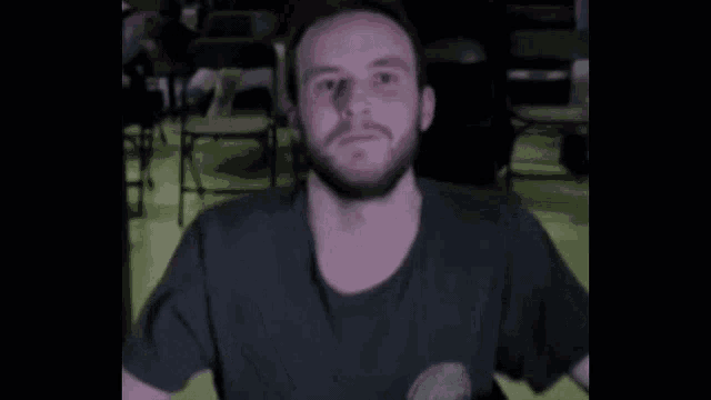 a man with a beard is sitting in a chair in a dark room with a chair in the background .
