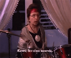 a woman is playing drums in front of a window with a caption in greek that says kavelc