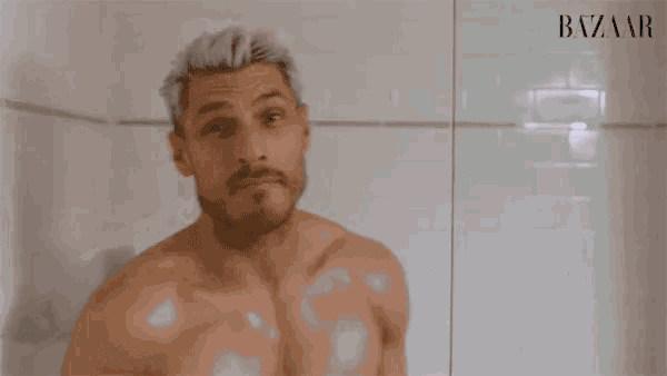 a man without a shirt is looking at himself in a mirror and the word bazaar is on the wall