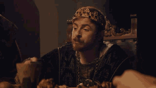 a man with a crown on his head is sitting at a table