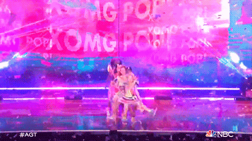 a group of people are dancing on a stage in front of a sign that says pop omg pop