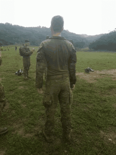 a man in a camouflage uniform stands in a grassy field