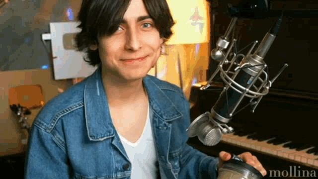 a man in a denim jacket is holding a microphone in front of a piano ..