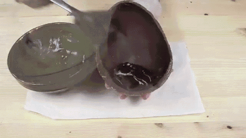 a chocolate egg is sitting on a wooden table next to a bowl filled with chocolate .
