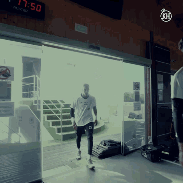 a man wearing a white shirt with the number 22 on it walks through a sliding glass door