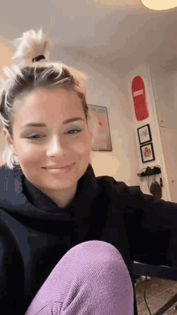 a woman in a black hoodie is smiling in front of a skateboard on the wall