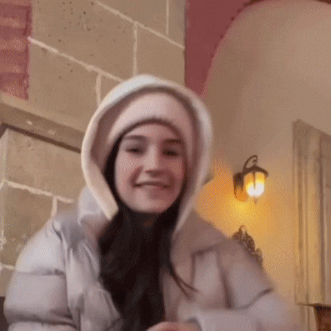 a woman wearing a hooded jacket and a pink hat is smiling and looking at the camera .