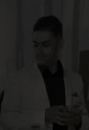 a man in a white suit and black shirt is holding a glass of wine in his hand .