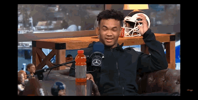 a man sitting in front of a microphone holding a football helmet and a gatorade bottle