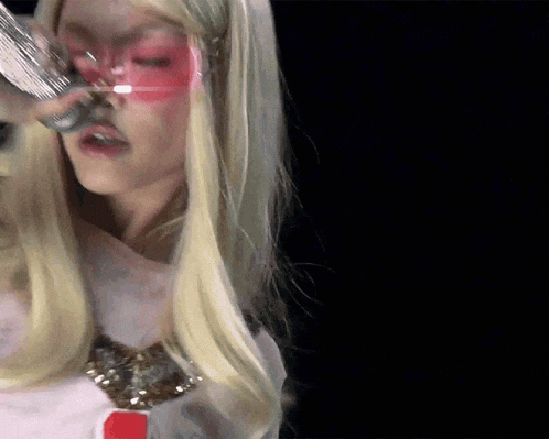 a woman with blonde hair and pink glasses is holding a silver object in her hand