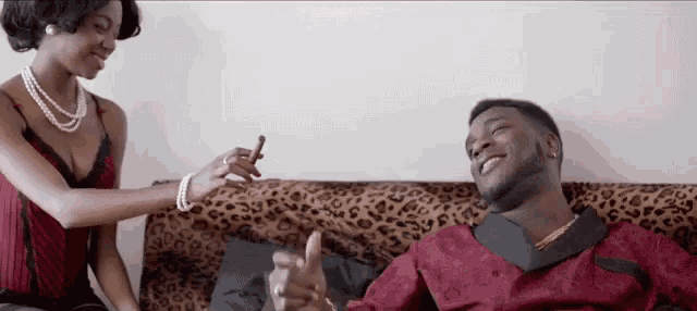 a man and a woman are sitting on a leopard print couch and the woman is giving the man a cigar