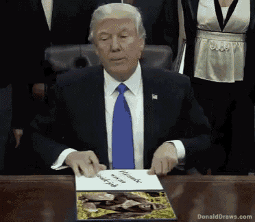 donald trump is sitting at a desk with a picture of a man holding a piece of paper that says thank you for your service
