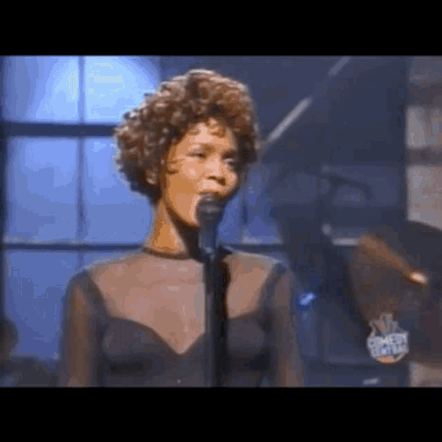 a woman in a black dress is singing into a microphone on stage .