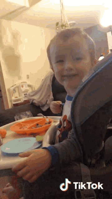 a little boy is sitting in a high chair with a tiktok logo on the bottom