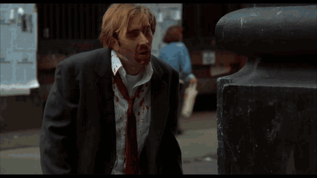 a man in a suit and tie with blood on his face says " what do you mean the both of us "