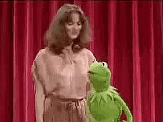 a woman is standing next to a green frog on a stage .
