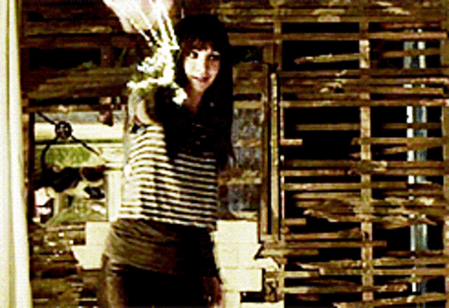 a woman in a striped shirt stands in front of a wooden fence
