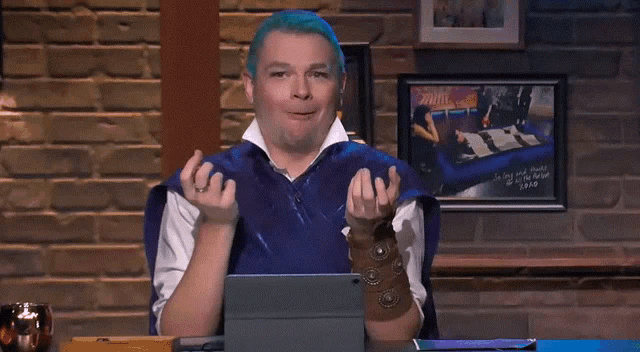 a man with blue hair is sitting in front of a brick wall with a framed picture that says ' junk ' on it