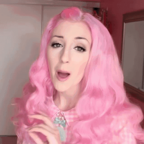 a woman with long pink hair is singing into a microphone in a room .