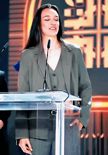 a woman in a suit stands behind a podium with her eyes closed