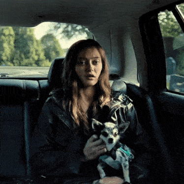 a woman is holding a small dog in her lap in a car