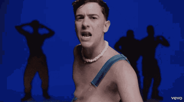 a shirtless man is smiling in front of a blue background with the word vevo on the bottom