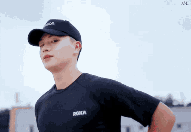 a man wearing a black t-shirt and a black hat with the word roka on it