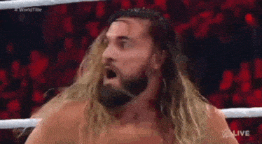 a wrestler with long blonde hair and a beard is standing in a wrestling ring .