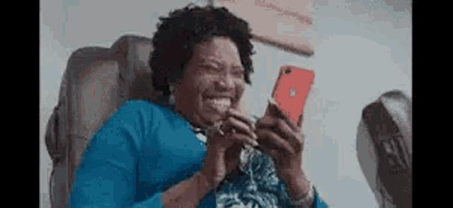a woman is sitting in a chair laughing while using a cell phone .