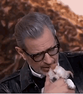 a man wearing glasses is holding a small white dog in his arms .