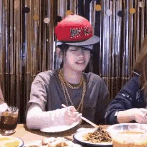 a man wearing a hat that says ' chicago bulls ' on it is sitting at a table eating spaghetti .