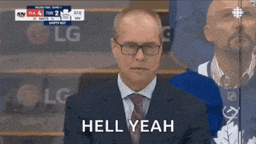 a man in a suit and tie is sitting in front of a hockey player and says hell yeah .