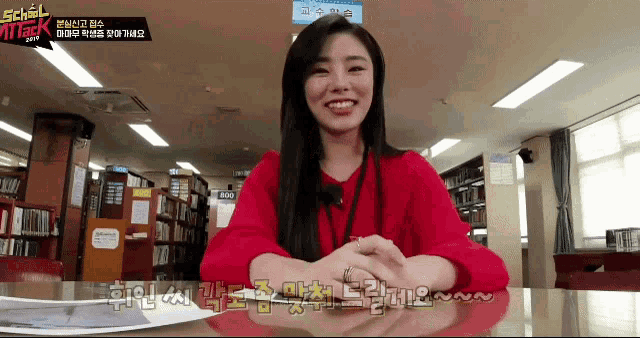 a woman in a red sweater sits at a desk in front of a sign that says school girl