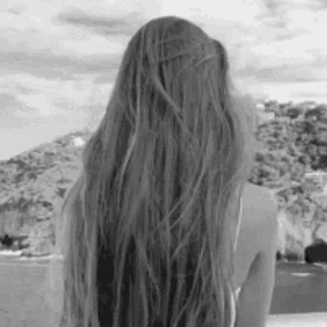 a black and white photo of a woman with very long hair looking at the ocean .