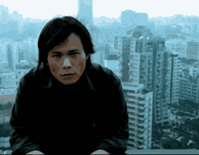 a man in a black jacket is sitting on a ledge overlooking a city