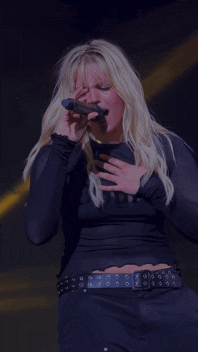 a woman singing into a microphone wearing a black shirt that says " built "