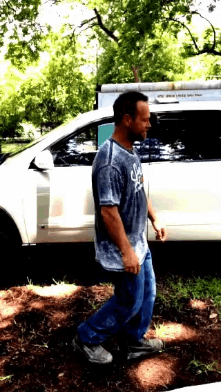 a man wearing a blue shirt with the letter s on it walks in front of a white van
