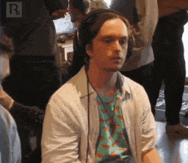 a man wearing headphones and a shirt with fish on it is sitting in a crowd