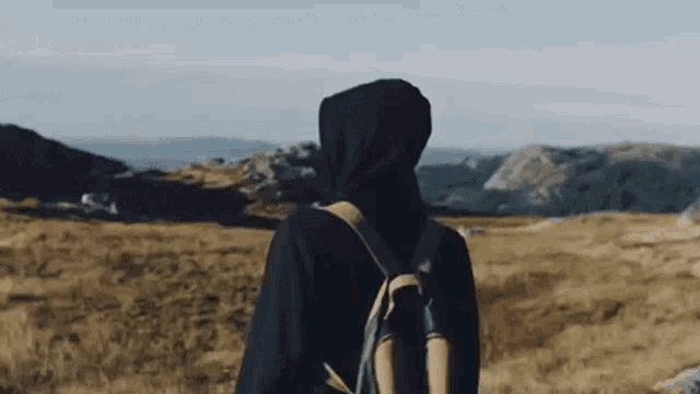 a person wearing a hooded jacket and a backpack is walking through a field .