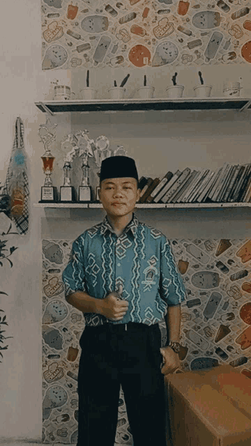 a young man in a blue shirt with a black hat stands in front of a shelf with trophies