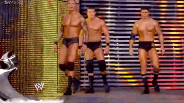 a group of wrestlers are standing on a stage in front of a wall with the letter w on it .