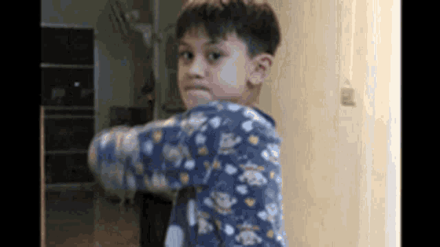 a young boy wearing a blue pajama top is standing in a room .