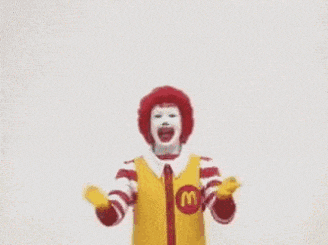 a mcdonald 's clown is holding up his arms in the air .
