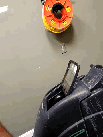 a yellow and orange spool of duct tape hangs on a wall above a black item
