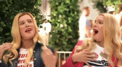 two blonde women are standing next to each other with their mouths open and their hands on their chests .