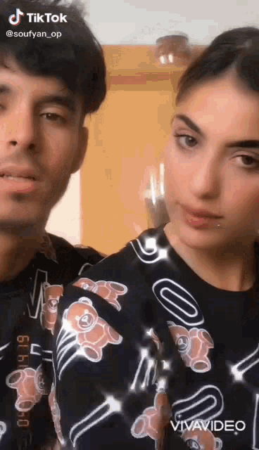 a man and a woman are standing next to each other and the woman is wearing a teddy bear shirt .