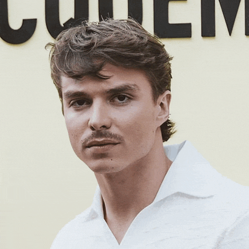 a man in a white shirt stands in front of a yellow wall with the word quemus on it