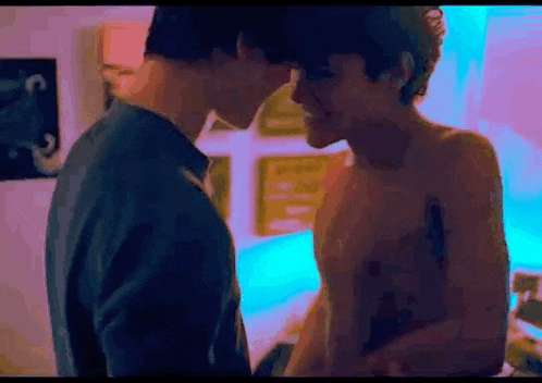 a couple of men are kissing in a room without shirts .